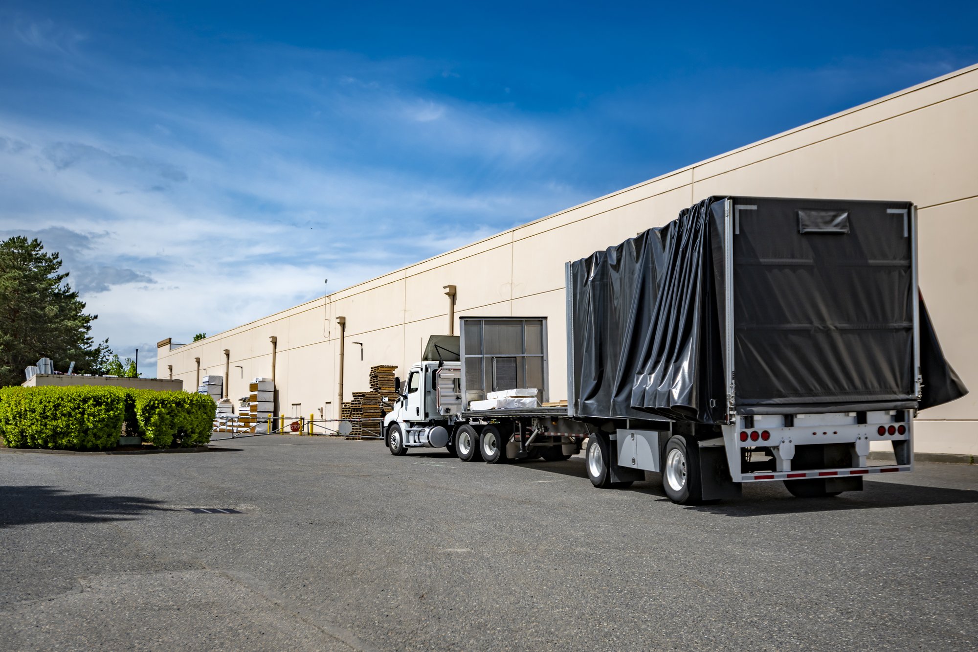 Flatbed truck with black coated fabric tarp at a distribution warehouse